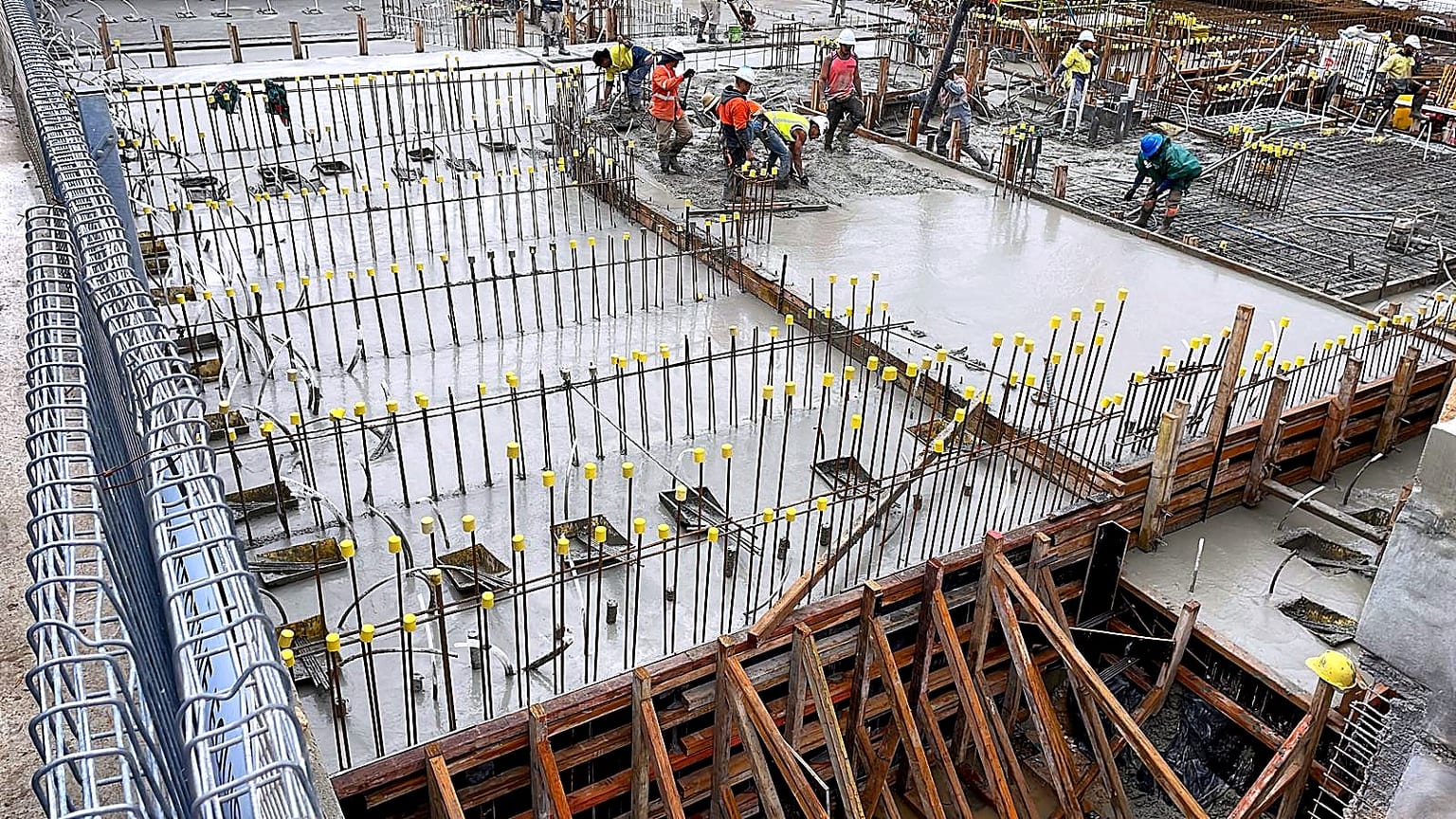 Workers finishing a concrete slab between wall reinforcement and timber edge forms.