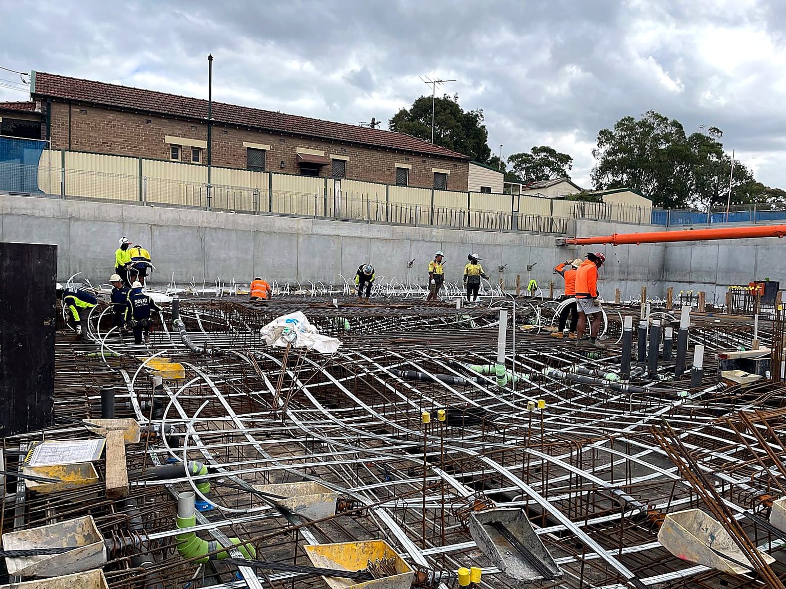 Site crew installing services and reinforcement across a basement slab before a concrete pour.
