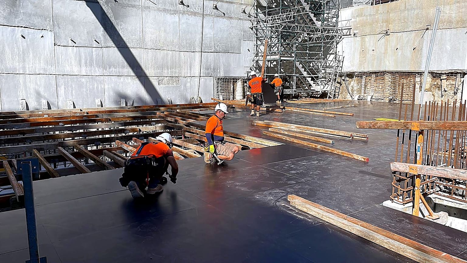 Formwork crew fixing black plywood deck panels over timber bearers in the basement.