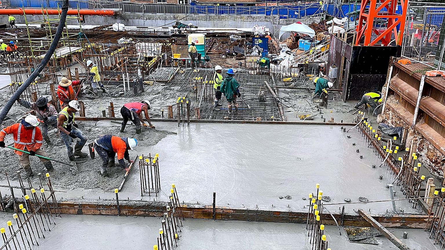 Site crew placing and levelling concrete across a reinforced basement slab.
