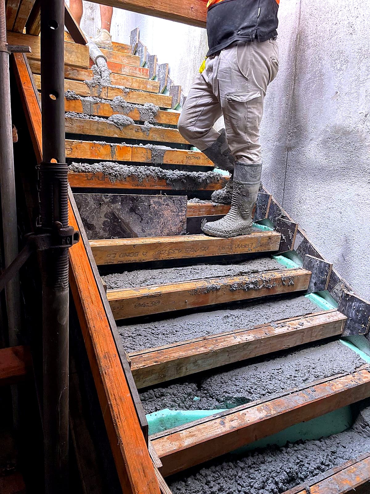 Worker standing on timber stair formwork as concrete is placed into the steps.