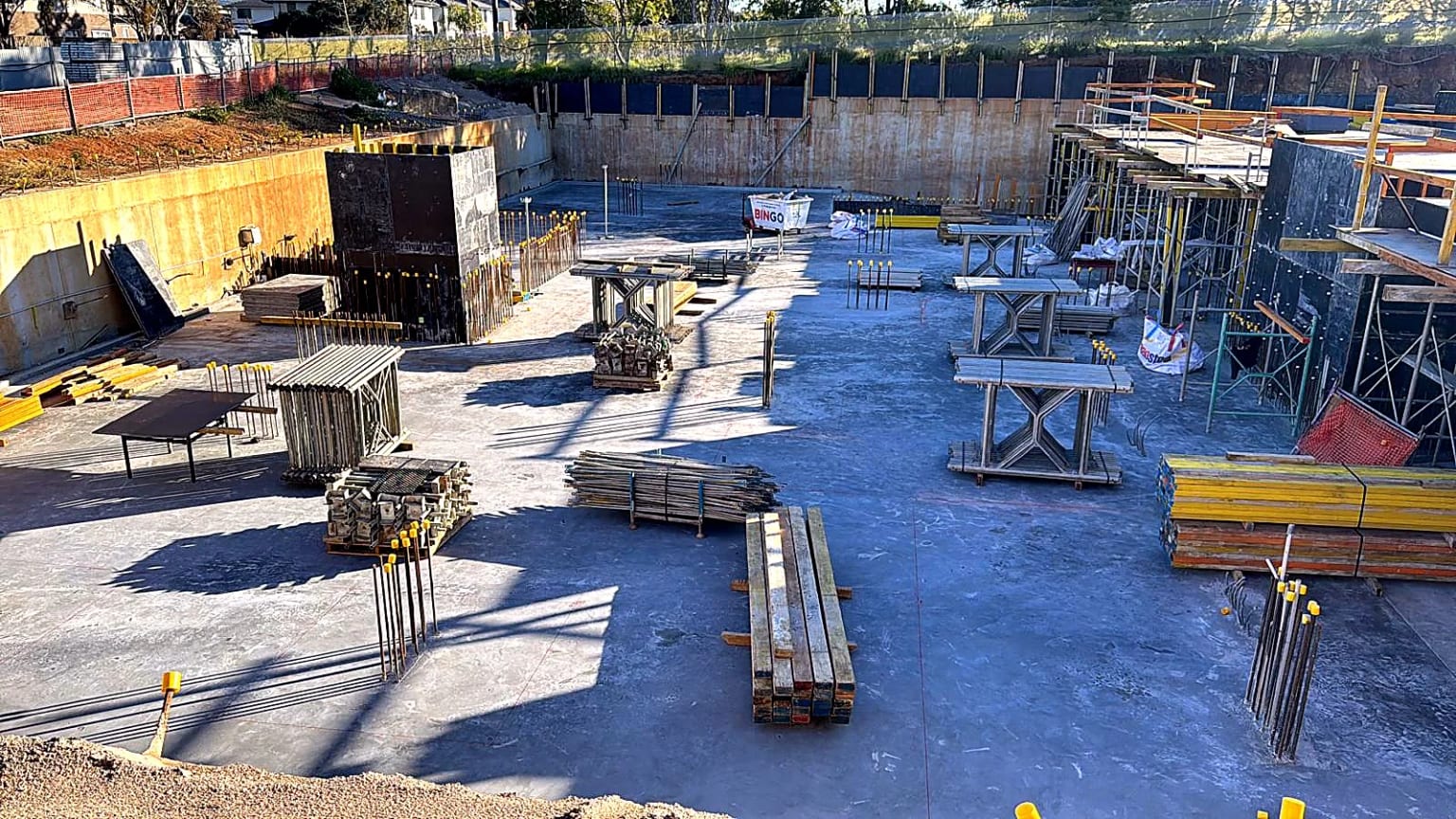 Formwork materials organised across the concrete base of an excavation.