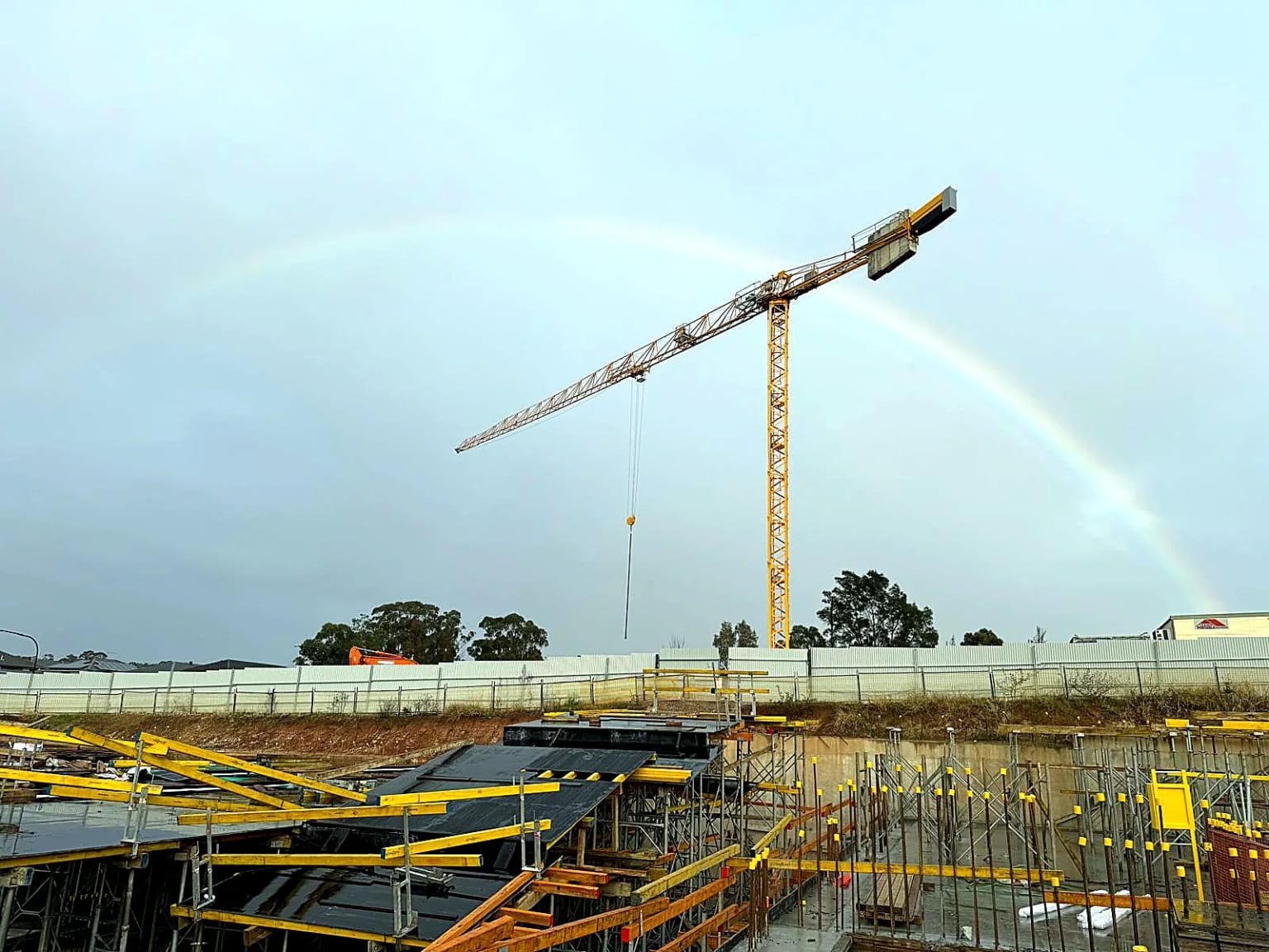 Tower crane above deck formwork with a rainbow in the background.