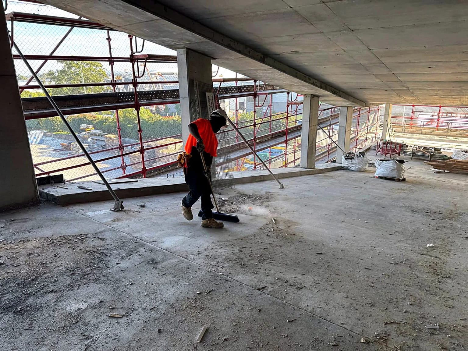 Worker clearing a completed concrete floor beside perimeter scaffolding.