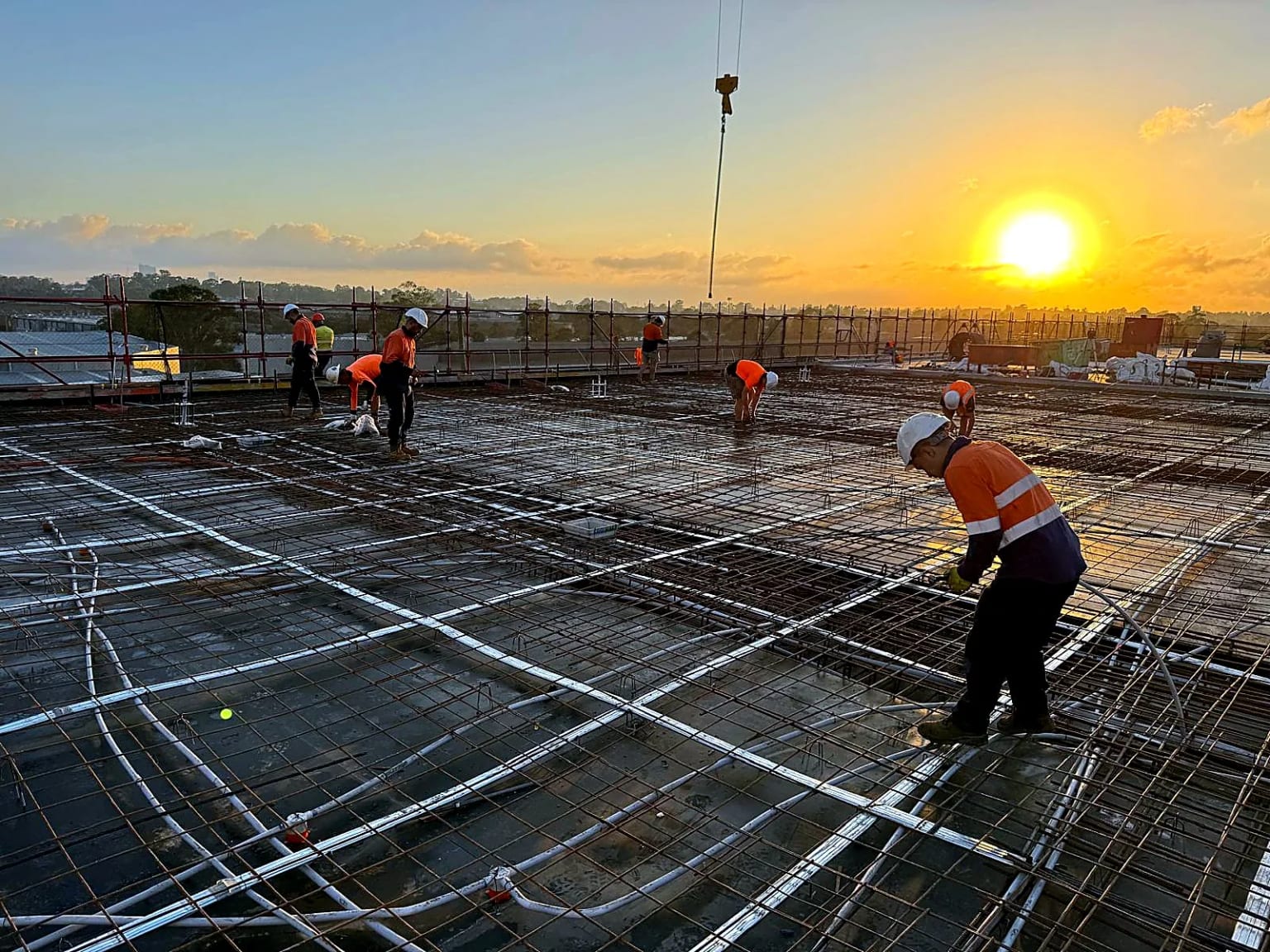 Site crew preparing slab reinforcement at sunset.