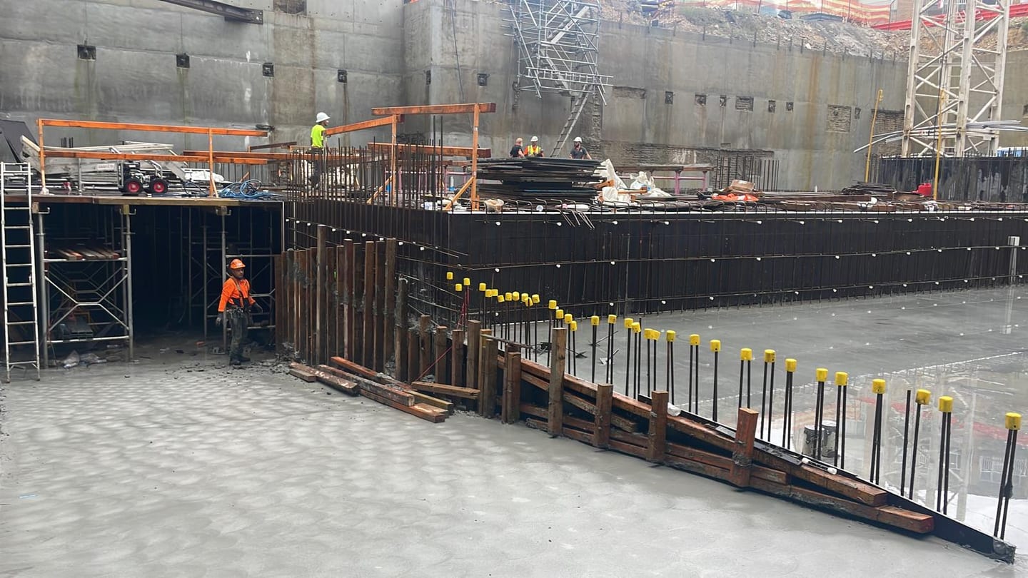 Concrete slab and reinforced walls under construction with formwork and site crew in a basement.