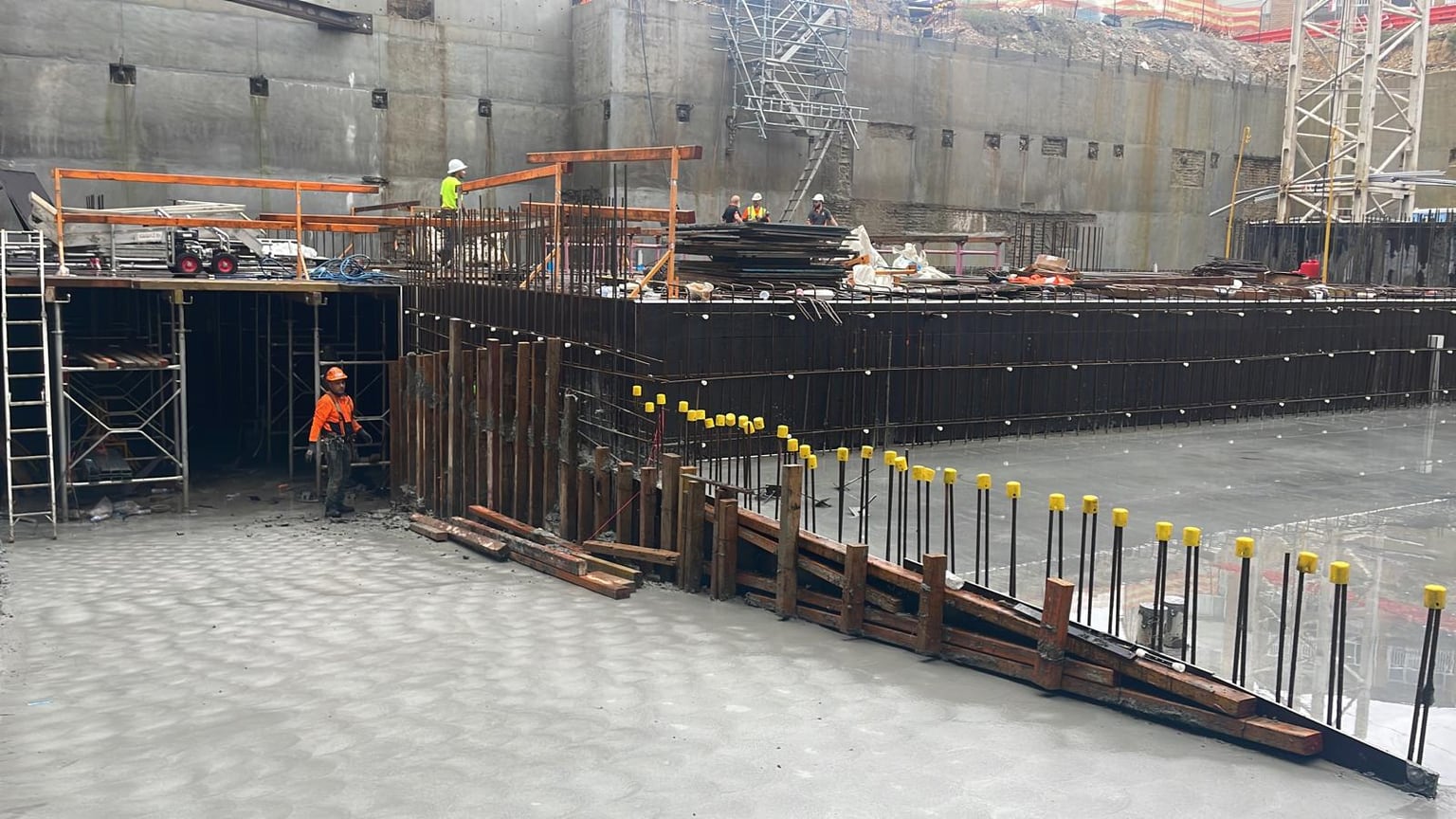 Concrete slab and reinforced walls under construction with formwork and site crew in a basement.