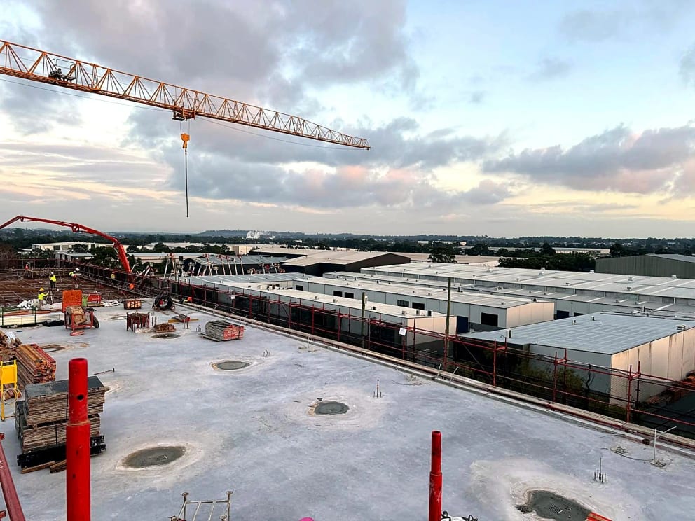 Tower crane and concrete pump above a completed slab and an active reinforcement area.